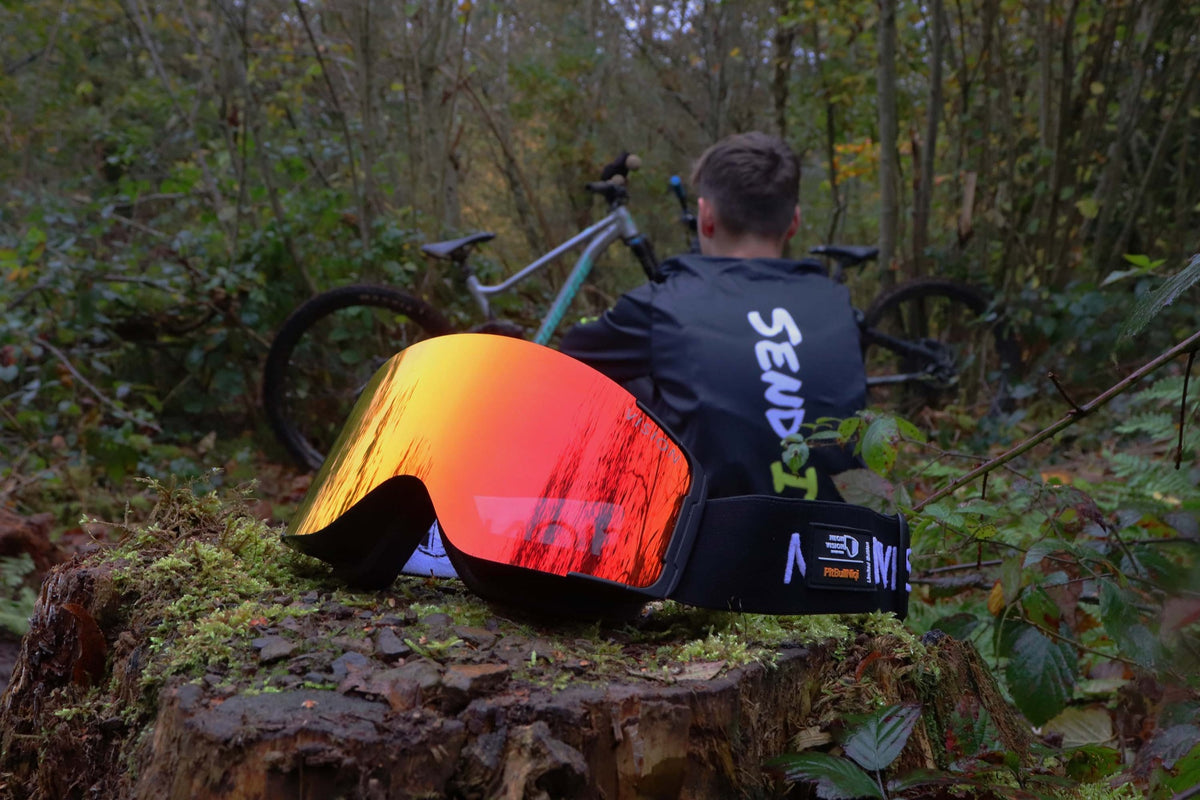 NeonVision FullFace Pro mit FireFly-Linse auf einem Baumstumpf im Wald, dahinter ein Fahrer mit Bike
